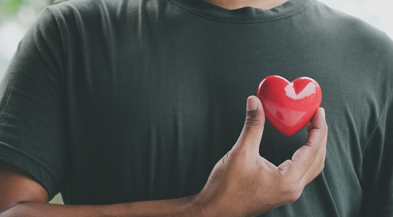 Man holding a heart in front of his chest, symbolizing love, and wellbeing.