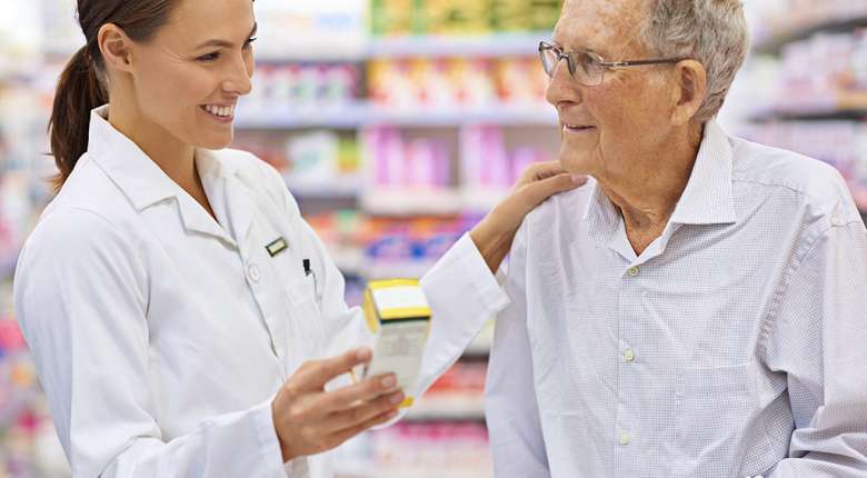 Pharmacist assisting an elderly customer with medication in a pharmacy aisle
