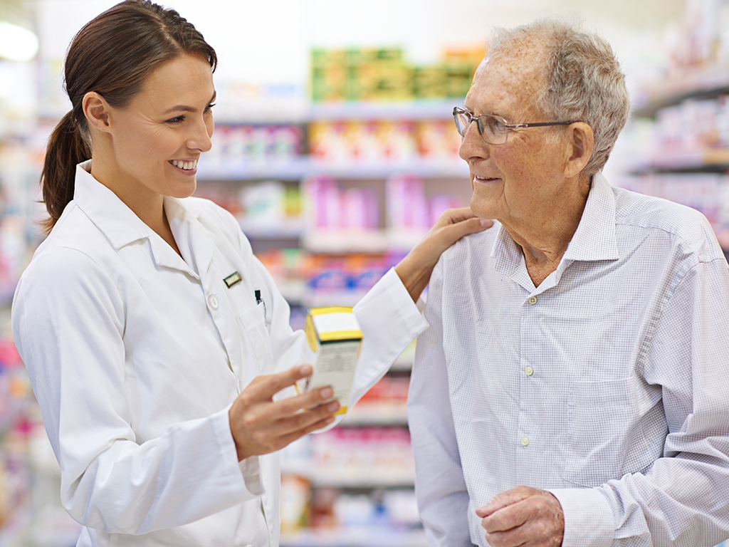 Pharmacist assisting an elderly customer with medication in a pharmacy aisle